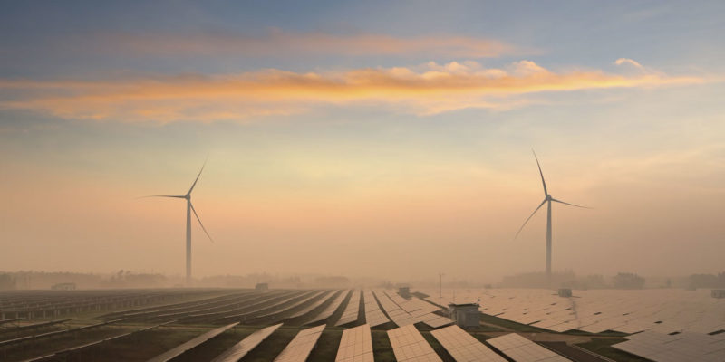 Blick auf Solaranlagen und Windräder vor gerötetem Himmel